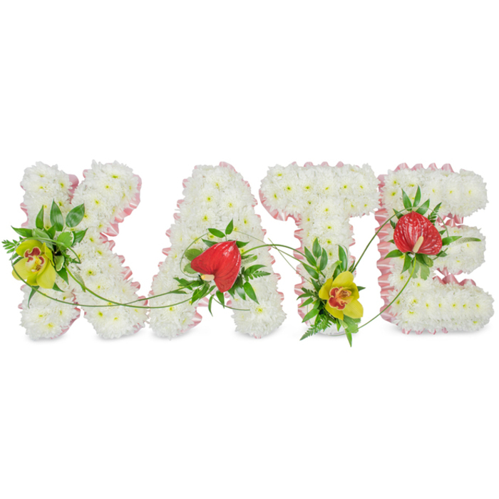 This photograph captures a refined floral name tribute spelling "KATE", crafted as a four-letter display typically placed beside the coffin or at the front of a funeral service around Loughton. Each capital letter is fully covered in tight clusters of white chrysanthemums, their petals forming a deep, cushiony texture that suggests softness and quiet support. Around the outer edge, a pale pink ribbon gently frames each letter, the slight shimmer of the satin adding elegance while the ruffled edging lends a tender, almost vintage charm, as if echoing a favourite dress or childhood keepsake. The florist has then added carefully balanced highlights of colour. On the "K" and "T", lime-tinged cymbidium orchids with warm red markings provide a sophisticated contrast to the white base, their sturdier petals rising slightly above the chrysanthemums. These are nestled into pockets of dark, glossy foliage and airy fern fronds, which bring natural movement and depth. On the "A" and "E", red anthuriums with pronounced heart shapes and a polished, waxy finish stand proudly, symbolising strong, enduring love amidst grief. Flowing strands of green vine meander across and between the letters, visually binding the name together and softening the overall outline. Against the simple white background, the tribute feels calm, composed, and deeply personal, as though made specifically for a cherished KATE from Loughton, perhaps someone who enjoyed walks through Epping Forest or visits to the High Road. The arrangement reflects the skill and sensitivity of an experienced local funeral florist, creating a bespoke sympathy piece that speaks quietly of remembrance and the bonds that remain.