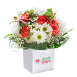 This bouquet radiates a spirit of cheerful abundance, thoughtfully arranged by florists in Loughton and presented upright within a crisp, modern white gift bag. Soft coral and bold red carnations, their petals layered with frilled delicacy, set a lively foundation, while bright white daisies punctuate the arrangement with bursts of joyful clarity-their lime-green centers echoing the vibrance of a spring morning in Loughton's local parks. Feathery baby's breath floats through the bouquet, its tiny white blooms adding a gently whimsical softness, and on the left edge, hints of purple-tinted buds lend a playful intrigue. The deep, smooth green leaves that cradle the base evoke the feel of Loughton's woodland edges, grounding the composition in nature's richness. Arranged in a perfect, generous dome, the bouquet feels intentional and generous-an ideal gift for birthdays, anniversaries, or brightening a home along Church Hill. The white bag features sturdy ribbon handles for effortless carrying, its front marked with a discreet logo connecting it back to Loughton's floral traditions. Set against a flawless white background, the entire scene embodies freshness and intention, capturing not just the beauty of the blooms, but also the thoughtful skill of a florist who knows the tastes and stories of their Loughton neighbours.